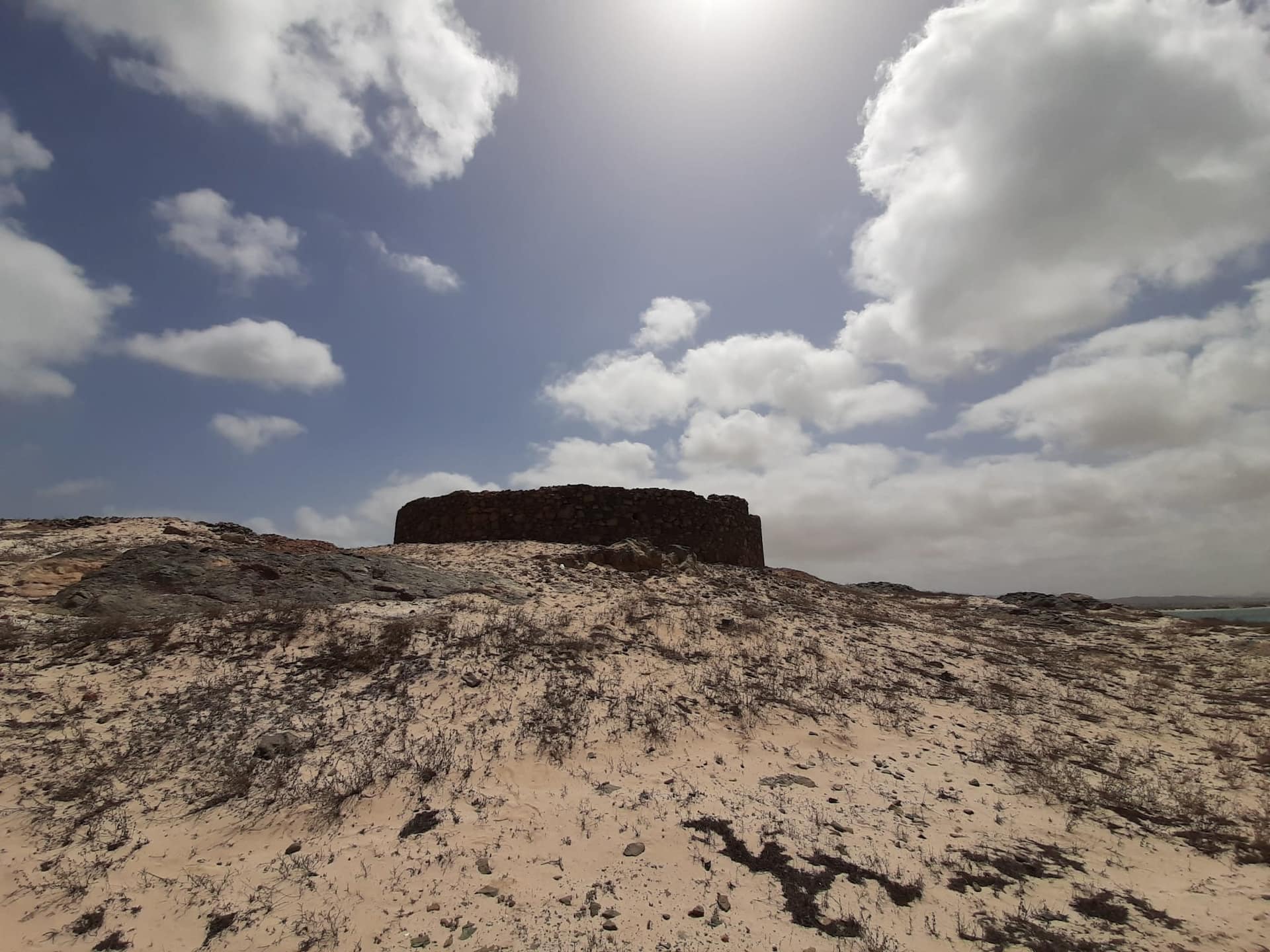 Forte Duque de Bragança do ilhéu de Sal Rei 1820 (c.). Fotografia de Luís B. de Sousa para arquipelagos.pt , 12 de julho de 2022 Ilha da Boa Vista, Cabo Verde. A Ilha da Boa Vista foi saqueada várias vezes, especialmente entre 1815 e 1817, por causa da sua importância para a exportação de sal, algodão, gado, cal e cerâmica, o que levou à transferência do principal núcleo urbano, na chamada Povoação Velha , para o antigo Porto Inglês , depois designado por Sal-Rei . De acordo com planta da Sociedade de Geografia de Lisboa de Ernesto de Andrada, de outubro de 1888, a vila terá sido fundada nos finais de Setecentos, sendo o seu fundador o capitão‐mor Aniceto António Ferreira, “ segundo a versão mais fundamentada e aceite “. Nessa sequência se investiu na sua defesa, com a construção do forte duque de Bragança , solicitado pelo governador António Pusich (c.1760-c. 1825), já nomeado pela corte portuguesa no Rio de Janeiro, e construção de 1820 a 1821 , como parece indiciar a denominação, ou seja, D. Pedro de Alcântara (1798-1834), príncipe herdeiro do reino unido de Portugal, Brasil e Algarves. A planta e o projeto parecem ter vindo do Rio de Janeiro e, provavelmente, com os mesmos, mestres calceteiros da ilha da Madeira, que haviam sido enviados para calcetar aquela cidade, pois que não conhecemos trabalhos semelhantes de calcetamento em Cabo Verde. Aquele governador, natural de Dubrovnick, na Cracóvia, em 1798 era responsável pelo brigue Dragão e, em 1799, já comandava o bergantim Balão , que nesse ano aportou às ilhas de Cabo Verde. Em 18 de março de 1801, foi nomeado intendente da Marinha de Cabo Verde e capitão-de-fragata graduado e, montada a corte portuguesa no Rio de Janeiro, foi governador de Cabo Verde de 6 de fevereiro 1818 a 1822 , mas já em setembro de 1821 regressara a Lisboa, face às alterações políticas, acompanhado da família, como a filha, depois a conhecida escritora e publicista, Antónia Gertrudes Pusich (1805-1883).