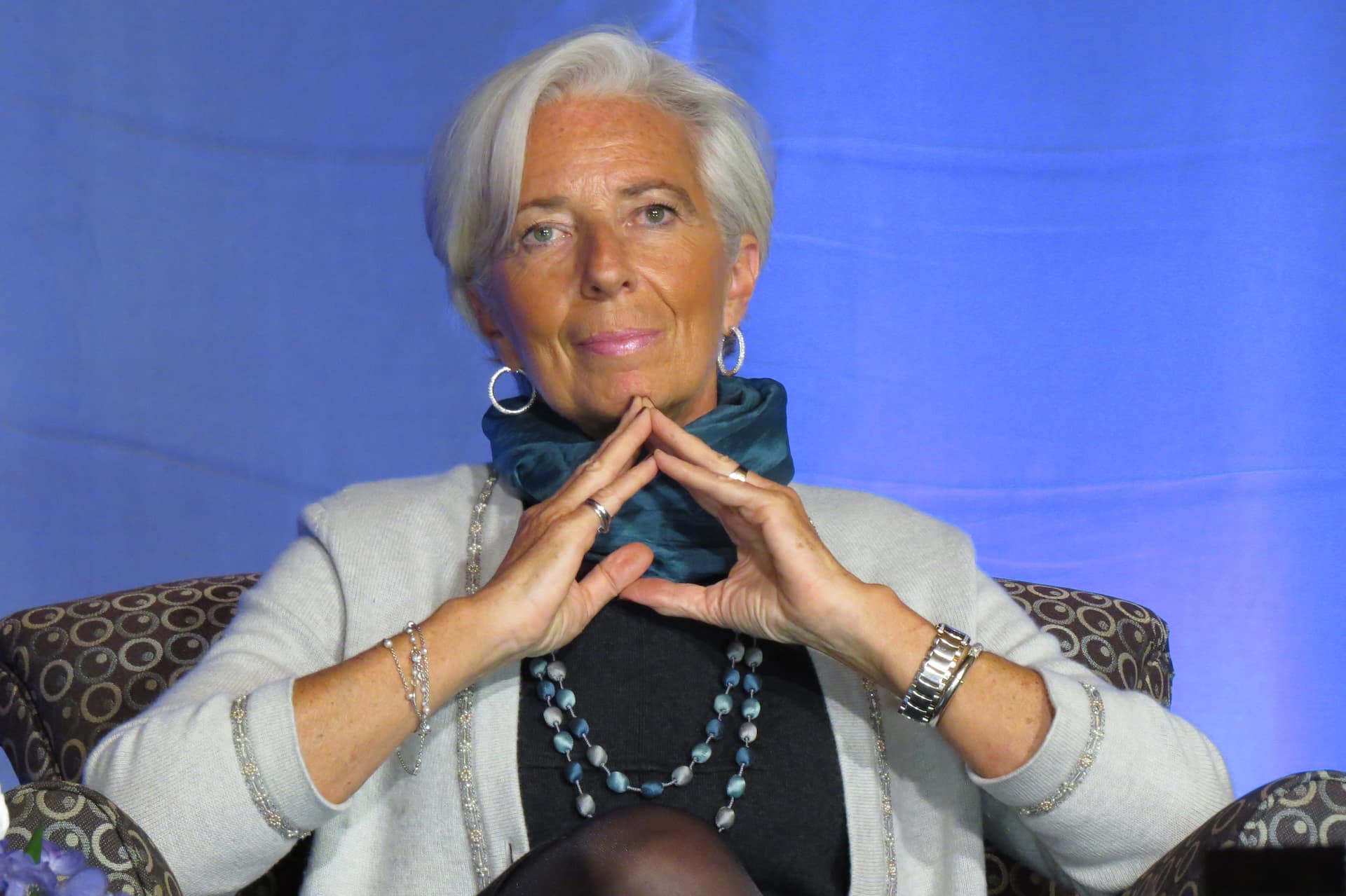 International Monetary Fund chief Christine Lagarde sits in a chair on stage at a public forum organized by the Madeleine Korbel Albright Institute for Global Affairs at Wellesley College. Lagarde made headlines for her declaration that economic "inequality is sexist." She makes a "Merkel-Raute" or "Triangle of Power" gesture with her hands.